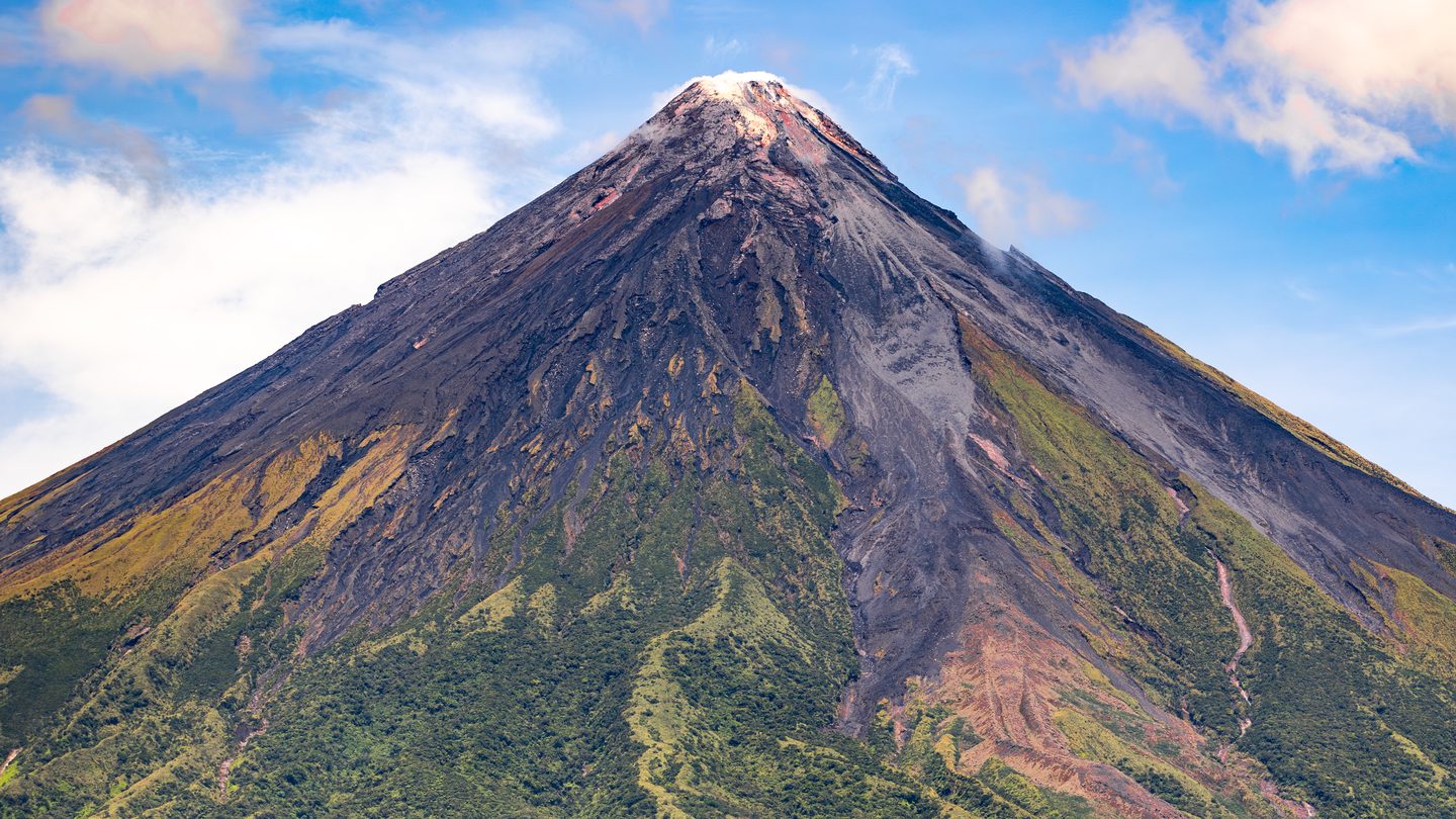 Mayon Volcano in the Philippines, a symmetric composite volcano cone rising from surrounding lowlands under a clear sky, widely cited as the world's most perfectly conical stratovolcano