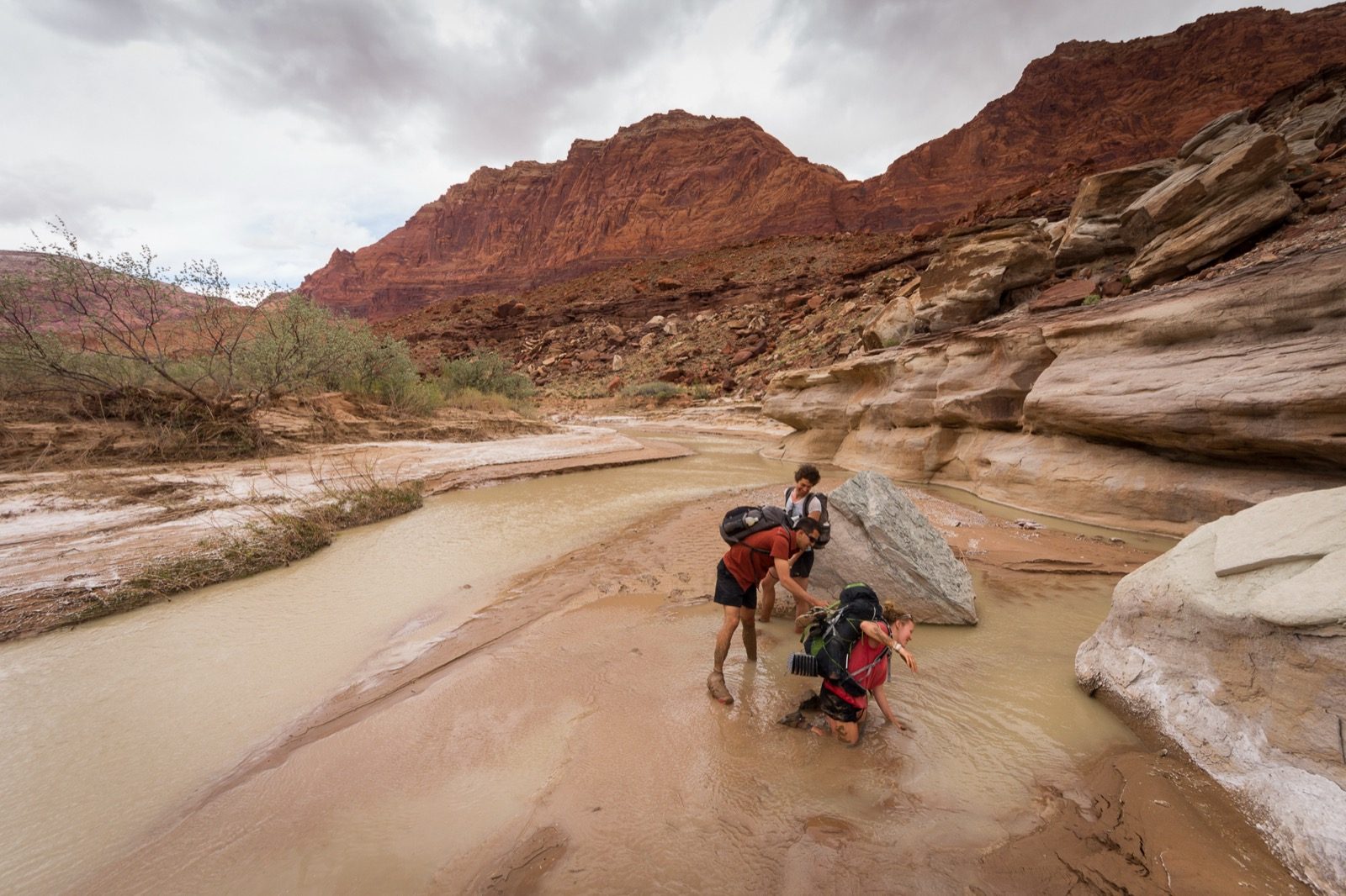 A person being pulled by two others out of a patch of quicksand near the Paria River, one leg still sunk into the sediment